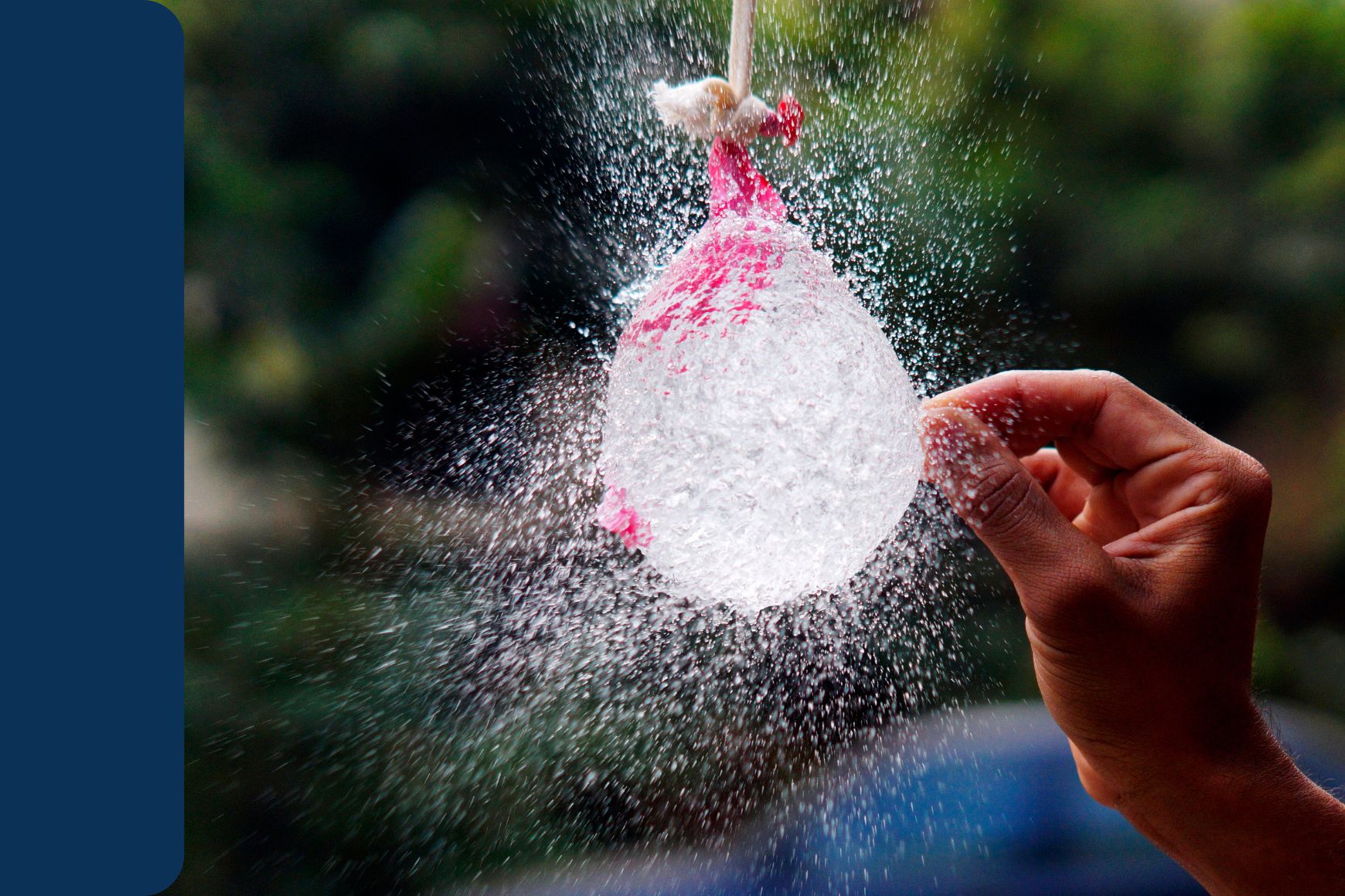 a water balloon burst by a hand holding a sharp pin